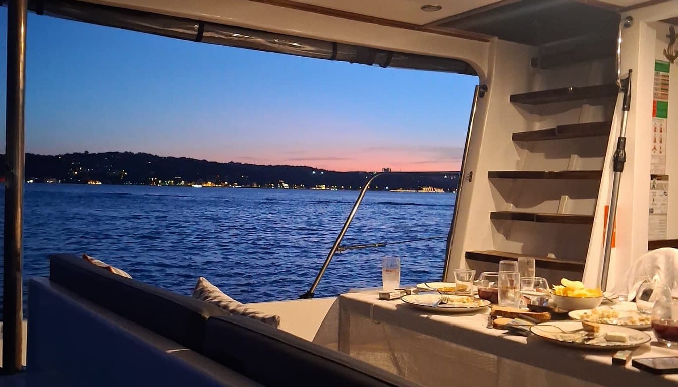İstanbul Boğazı'nda tarihi yalılar ve köprü önünde ilerleyen küçük butik özel tekne, gün batımı ışığında ahşap güverte